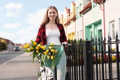 Beautiful teenage girl with bicycle and bouquet of yellow tulips on city street