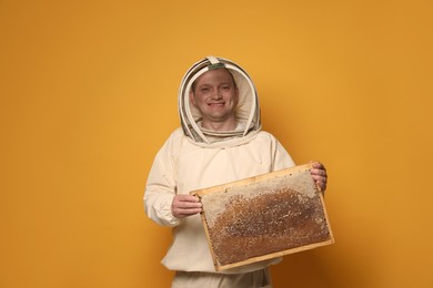 Beekeeper in uniform holding hive frame with honeycomb on yellow background