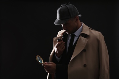 Old fashioned detective with smoking pipe and magnifying glass on dark background
