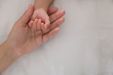 Mother with her baby on bed, closeup of hands. Space for text