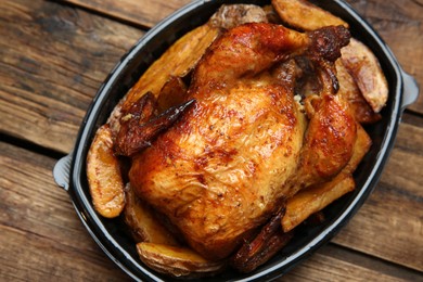 Delicious grilled whole chicken with potato in plastic container on wooden table, top view. Food delivery service