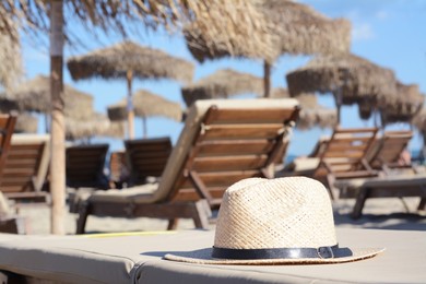 Stylish straw hat on sunbed at beach, space for text