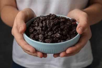 Woman holding bowl with raisins on black background, closeup