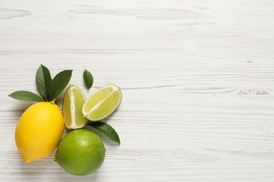 Fresh ripe lemon, limes and green leaves on white wooden background, flat lay. Space for text
