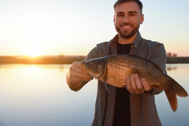 Photo of Fisherman holding caught fish at riverside. Recreational activity