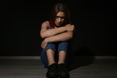 Abused young woman on black background. Domestic violence concept