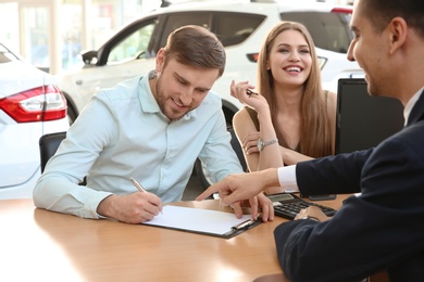 Young couple and salesman sitting at table in car salon. Buying auto