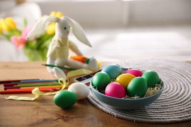 Bright painted Easter eggs, color pencils and toy bunny on wooden table indoors