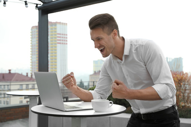 Emotional businessman working with laptop in outdoor cafe. Corporate blog