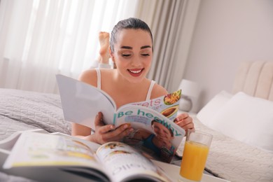 Happy woman reading magazine on bed indoors