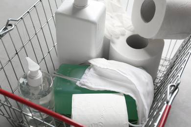 Shopping basket with antiseptics, toilet paper, gloves and masks on grey table, closeup. Panic caused by virus