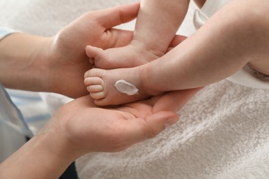 Mother applying body cream on her little baby indoors, closeup