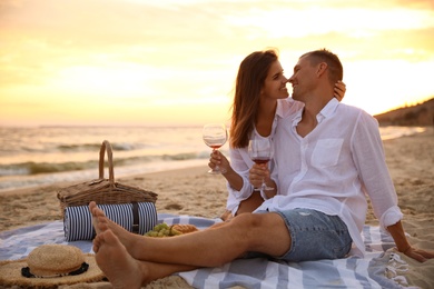 Lovely couple having romantic picnic on beach at sunset