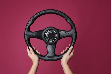 Woman holding steering wheel on crimson background, closeup
