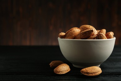 Ceramic bowl with almonds on black wooden table, space for text. Cooking utensil