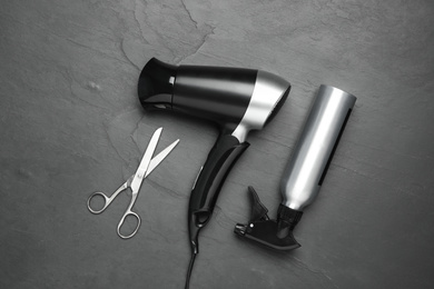 Hair dryer and professional hairdresser tools on black background, flat lay
