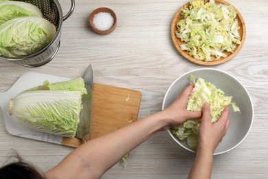 Woman putting cut Chinese cabbage into bowl at white wooden kitchen table, top view