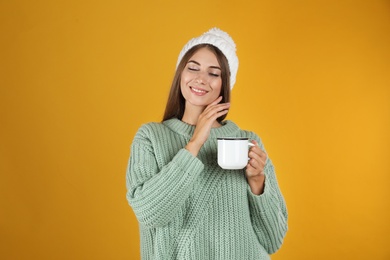 Happy beautiful woman with mug of mulled wine on yellow background