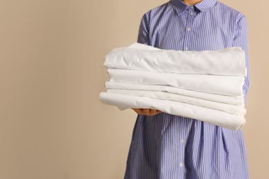 Woman holding stack of clean bed linens on beige background. Space for text