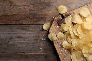 Board with delicious crispy potato chips on wooden table, top view. Space for text