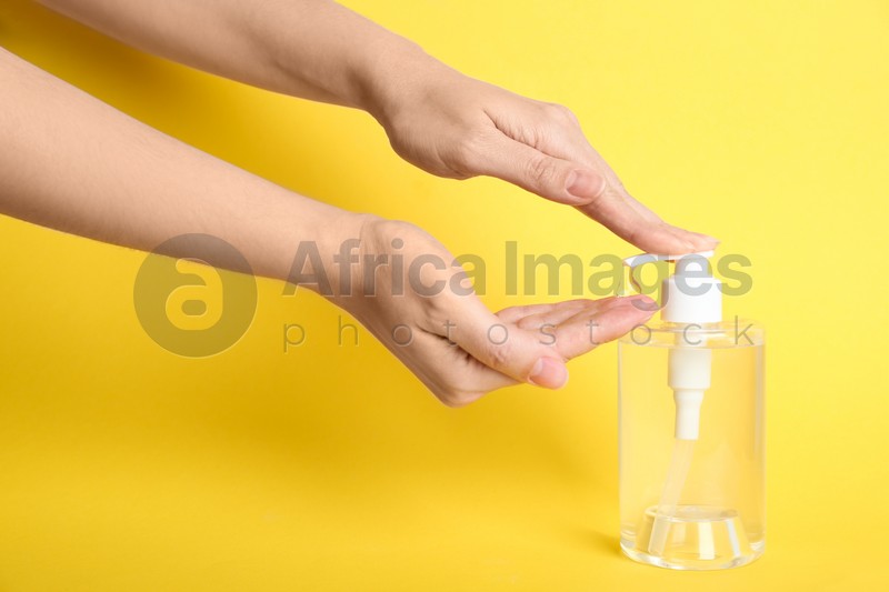 Woman applying antiseptic gel on hand against yellow background, closeup