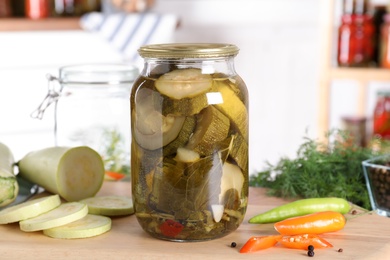 Jar with pickled zucchinis on wooden board indoors