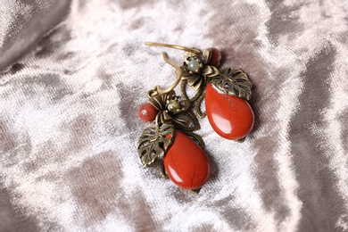 Beautiful pair of metal earrings with red jasper gemstones on light fabric