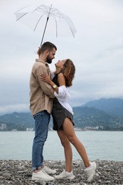 Photo of Young couple with umbrella enjoying time together under rain on beach