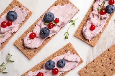 Tasty cracker sandwiches with cream cheese, blueberries, red currants and thyme on white marble board, flat lay