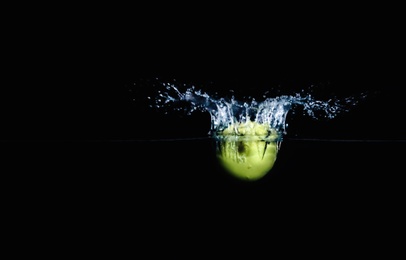 Ripe green apple falling down into clear water with splashes against black background