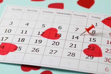 Calendar page with pin on Valentine's Day and hearts against turquoise background