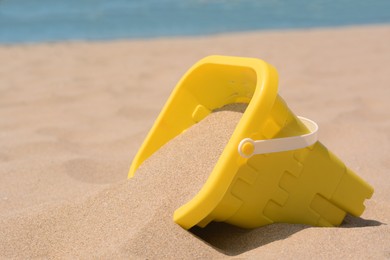 Yellow plastic bucket on sand near sea, closeup. Beach toy