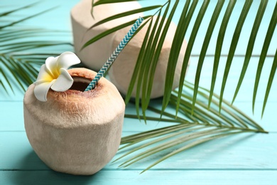 Young peeled coconuts with palm leaves and flower on light blue wooden table