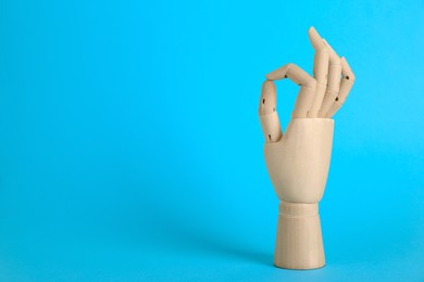 Photo of Wooden mannequin hand showing okay gesture on light blue background. Space for text