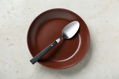 Photo of Empty brown ceramic plate with spoon on light grey table, top view