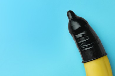 Banana with condom on light blue background, top view and space for text. Safe sex concept