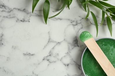 Spatula with wax and leaves on white marble table, flat lay. Space for text