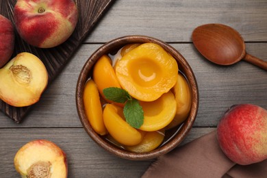 Canned peach halves in bowl on wooden table, flat lay