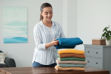 Young woman folding clothes at wooden table indoors
