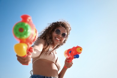 African American woman with water guns against blue sky, low angle view