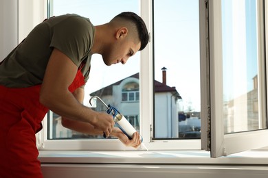Construction worker sealing window with caulk indoors