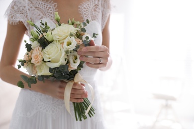 Young bride with beautiful wedding bouquet in room, closeup. Space for text
