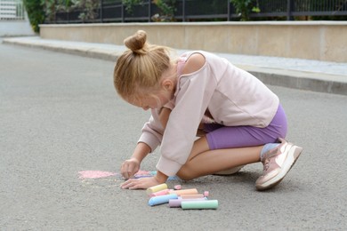 Photo of Little child drawing butterfly and heart with chalk on asphalt
