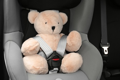 Teddy bear in child safety seat inside car. Danger prevention