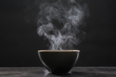 Steaming ceramic bowl on grey table against dark background