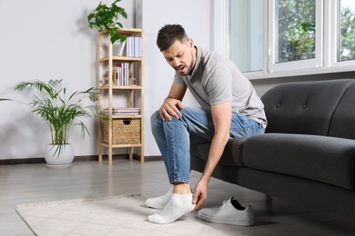 Man suffering from foot pain at home, space for text