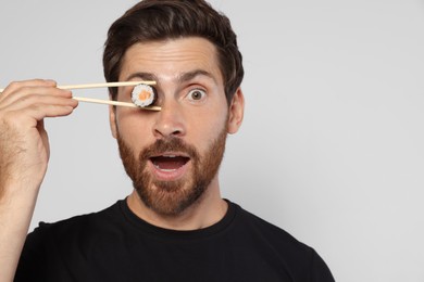 Photo of Funny man hiding his eye with sushi roll on light grey background. Space for text
