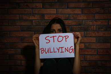Abused teen girl with sign STOP BULLYING near brick wall