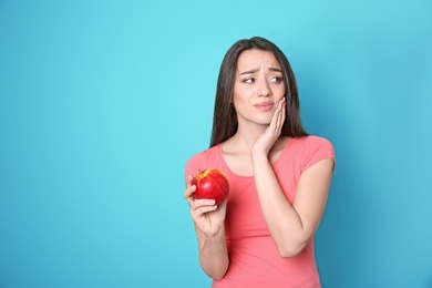 Woman with sensitive teeth holding apple on color background