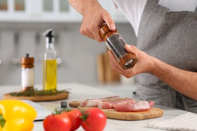 Man peppering steak at table in kitchen, closeup. Online cooking course